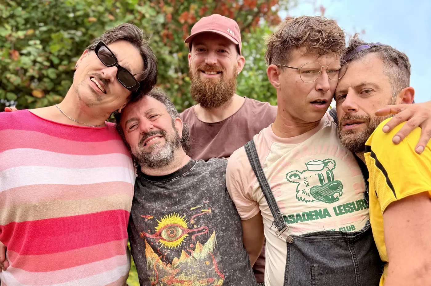 Five Kindred Faeries facilitators leaning into each other outdoors, laughing, in front of autumn trees